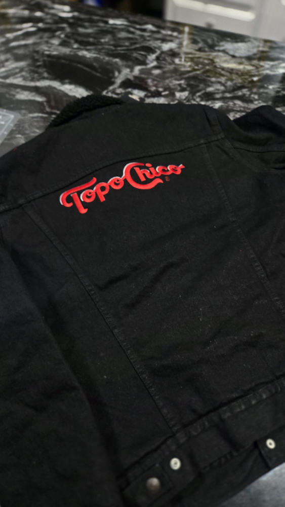 Topo Chico logo embroidered on the back of a black denim jacket